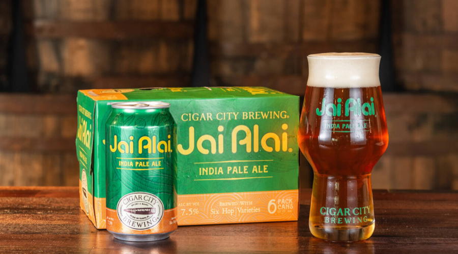 Cigar City Jai Alai 6-pack of cans and full pint glass in a barrel room