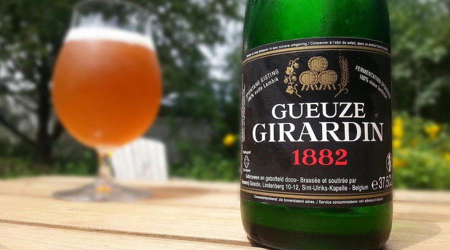 a bottle of Girardin Gueze 1882 black label and a glass on a table outside
